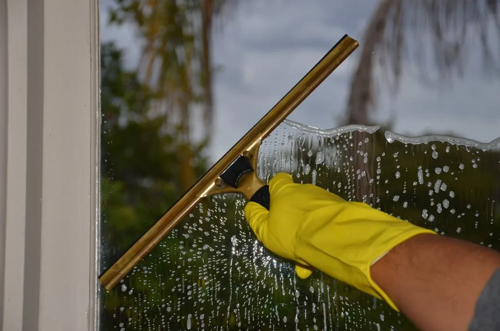 main gantée utilisant un squeegee pour nettoyer une fenêtre